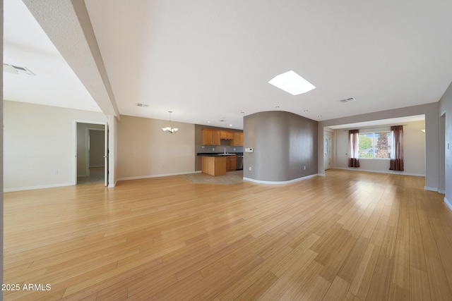 unfurnished living room featuring light wood-style floors, visible vents, baseboards, and a notable chandelier