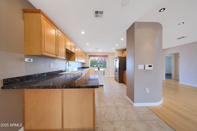 kitchen with visible vents, freestanding refrigerator, a sink, dark stone countertops, and a peninsula