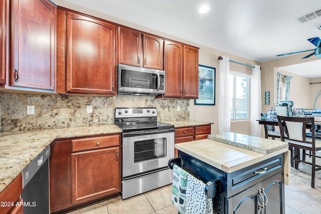 kitchen featuring light stone countertops, appliances with stainless steel finishes, backsplash, ceiling fan, and light tile floors