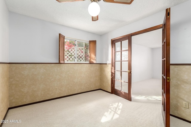 carpeted empty room featuring ceiling fan, a textured ceiling, and french doors