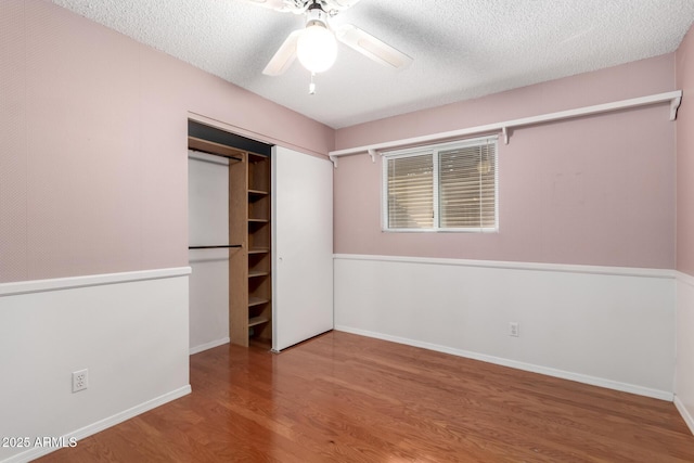 unfurnished bedroom featuring ceiling fan, a closet, hardwood / wood-style floors, and a textured ceiling