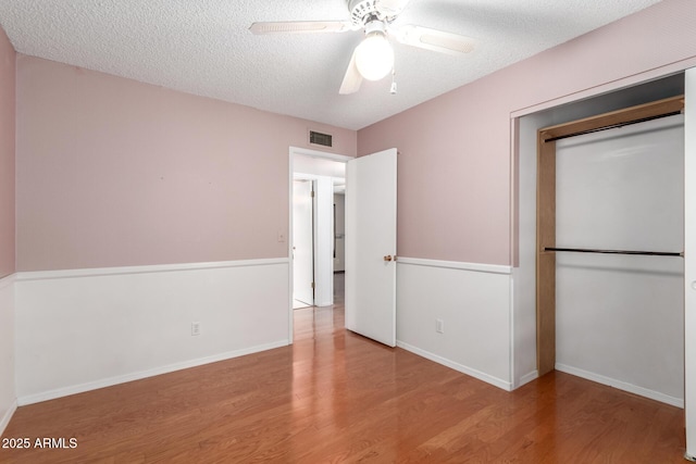 unfurnished bedroom with ceiling fan, a closet, light hardwood / wood-style floors, and a textured ceiling