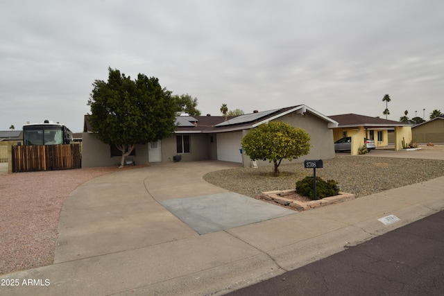 single story home with fence, stucco siding, concrete driveway, a garage, and roof mounted solar panels