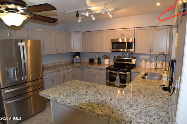 kitchen with light stone counters, stainless steel appliances, kitchen peninsula, and sink