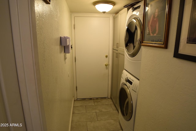 clothes washing area featuring cabinets, stacked washer / drying machine, and light tile patterned floors