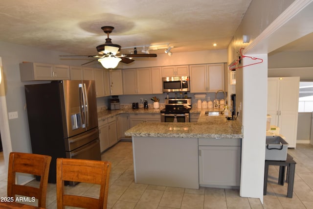 kitchen featuring sink, appliances with stainless steel finishes, kitchen peninsula, ceiling fan, and light stone countertops