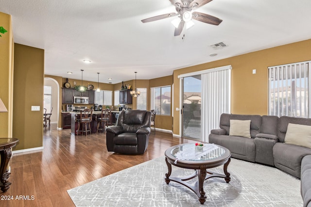 living room featuring ceiling fan with notable chandelier, dark hardwood / wood-style flooring, and a wealth of natural light