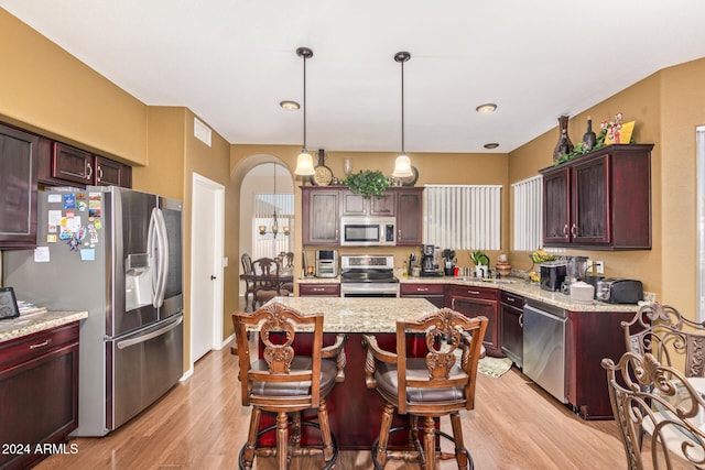 kitchen with light stone countertops, appliances with stainless steel finishes, light wood-type flooring, pendant lighting, and a kitchen island