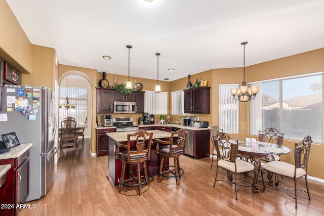 kitchen featuring appliances with stainless steel finishes, pendant lighting, an inviting chandelier, light hardwood / wood-style flooring, and a center island