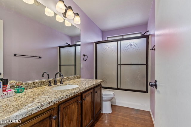 full bathroom with bath / shower combo with glass door, vanity, wood-type flooring, and toilet