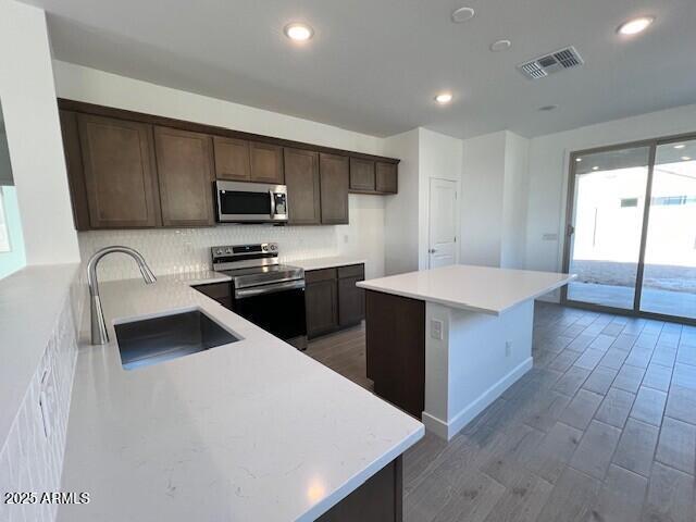 kitchen featuring sink, light hardwood / wood-style flooring, appliances with stainless steel finishes, a kitchen island, and decorative backsplash