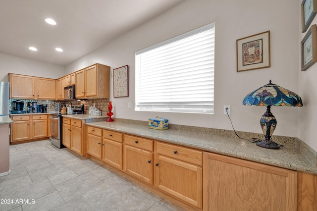 kitchen with light brown cabinets, light stone counters, stainless steel appliances, and tasteful backsplash