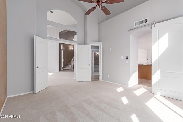 spare room featuring visible vents, light colored carpet, stairs, a high ceiling, and arched walkways