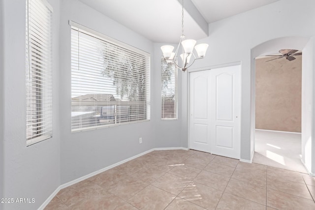 unfurnished dining area featuring light tile patterned floors, baseboards, arched walkways, and ceiling fan with notable chandelier