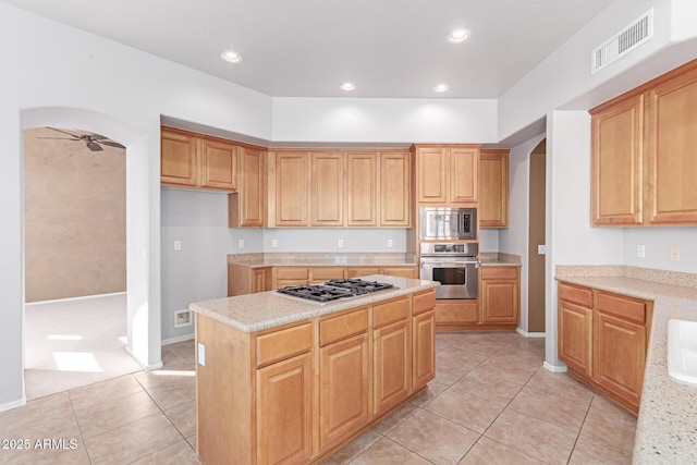 kitchen featuring visible vents, a center island, arched walkways, stainless steel appliances, and a ceiling fan