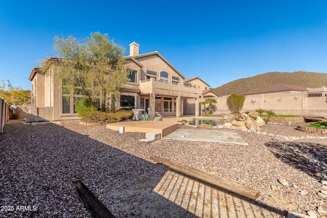 back of house with stucco siding, a chimney, a fenced backyard, a balcony, and a patio