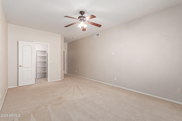 unfurnished bedroom featuring visible vents, a walk in closet, ceiling fan, baseboards, and light carpet