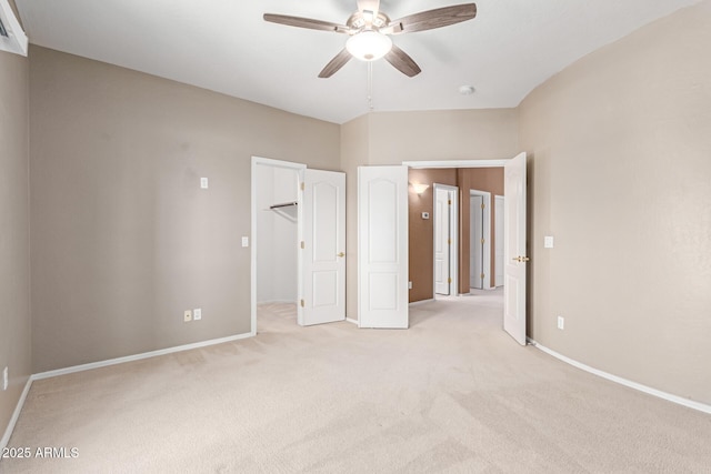 unfurnished bedroom featuring light carpet, ceiling fan, a spacious closet, and baseboards