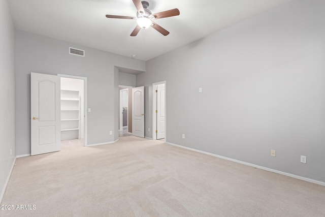 unfurnished bedroom featuring a walk in closet, ceiling fan, baseboards, light carpet, and ensuite bathroom