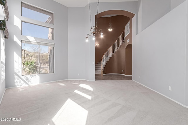 unfurnished living room with arched walkways, carpet flooring, a high ceiling, and an inviting chandelier