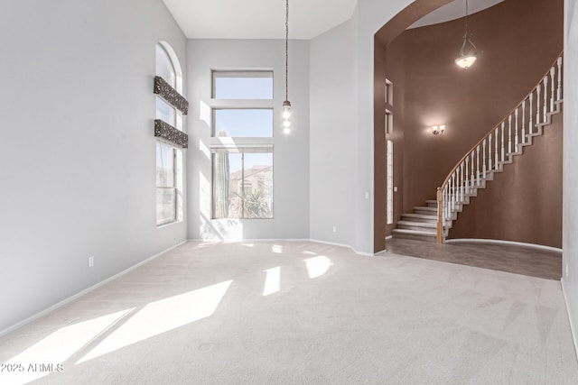 interior space featuring baseboards, carpet floors, a towering ceiling, and stairs