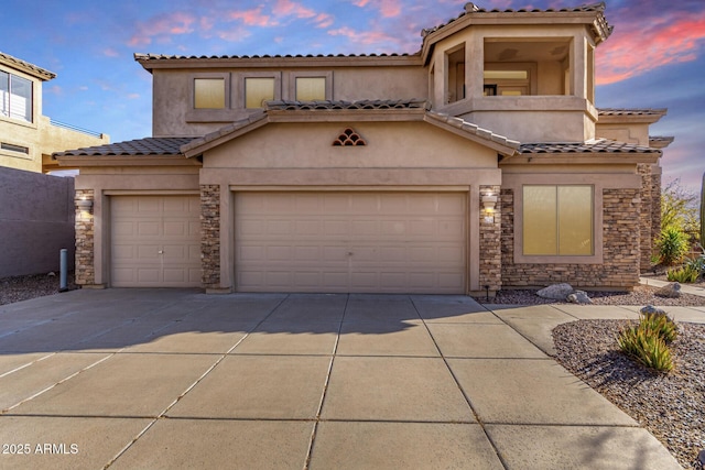 mediterranean / spanish-style home featuring driveway, an attached garage, stucco siding, stone siding, and a tile roof