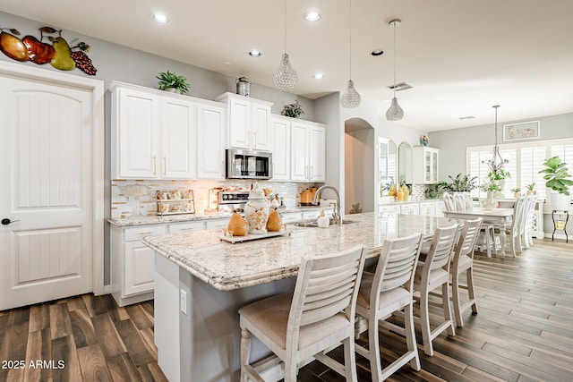 kitchen featuring a center island with sink, white cabinetry, hanging light fixtures, and sink