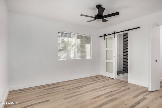 unfurnished bedroom with a barn door, light hardwood / wood-style flooring, and ceiling fan