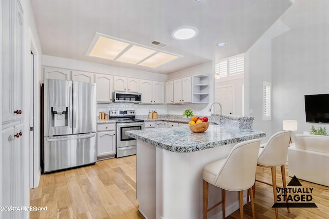 kitchen with a kitchen breakfast bar, kitchen peninsula, white cabinetry, and appliances with stainless steel finishes