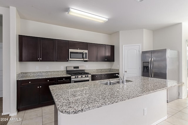 kitchen with a center island with sink, stainless steel appliances, light tile patterned floors, dark brown cabinetry, and sink