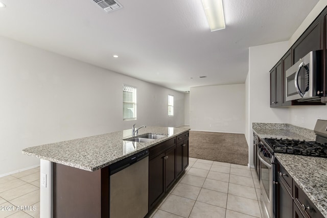 kitchen with a center island with sink, stainless steel appliances, dark brown cabinets, light carpet, and sink