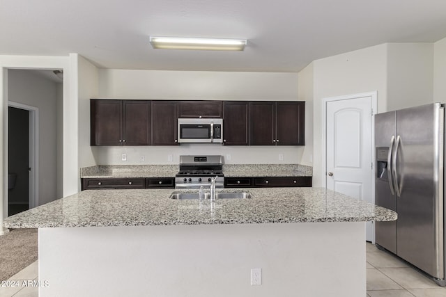 kitchen featuring a kitchen island with sink, stainless steel appliances, light tile patterned flooring, and dark brown cabinets