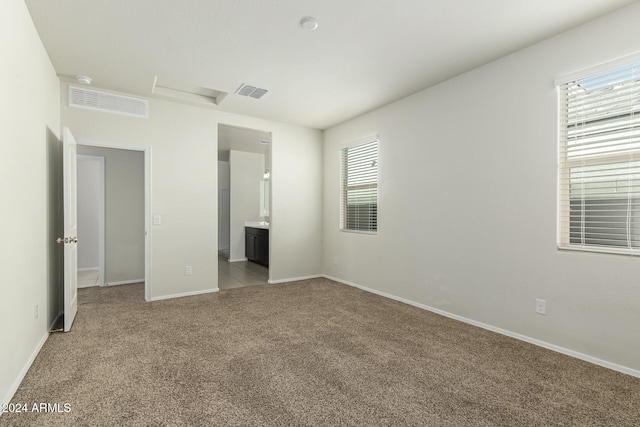 unfurnished bedroom with multiple windows, light carpet, and ensuite bath