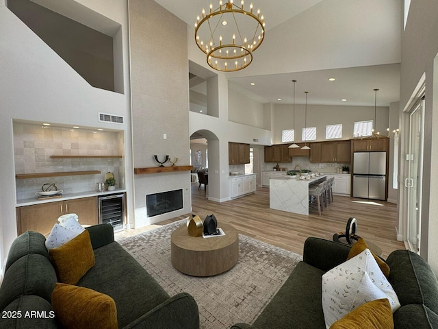 living room with arched walkways, light wood-style flooring, beverage cooler, visible vents, and a glass covered fireplace