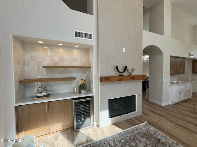 living room with light wood finished floors, visible vents, arched walkways, a towering ceiling, and wine cooler