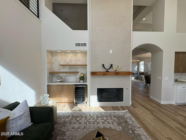 unfurnished living room featuring beverage cooler, light wood finished floors, a towering ceiling, and visible vents