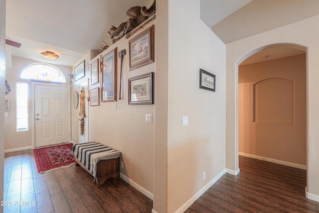 foyer entrance featuring arched walkways, dark wood finished floors, and baseboards