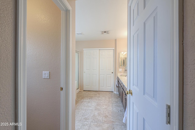 bathroom featuring stone finish flooring, visible vents, a textured wall, and vanity