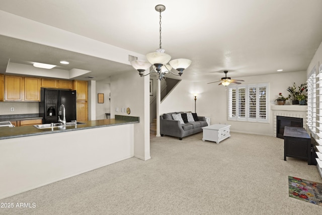 kitchen featuring sink, black fridge, decorative light fixtures, light carpet, and ceiling fan with notable chandelier