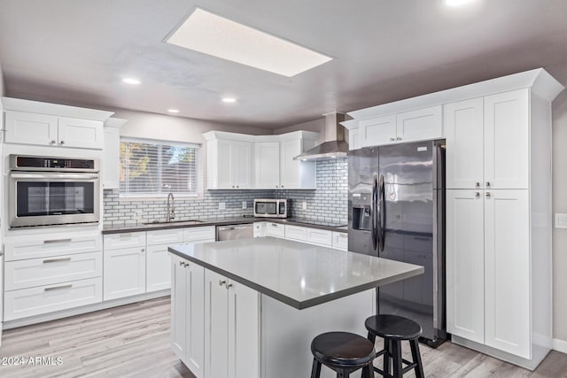kitchen featuring white cabinetry, stainless steel appliances, wall chimney exhaust hood, and a sink