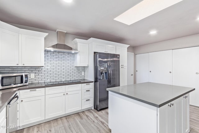 kitchen with dark countertops, wall chimney range hood, light wood-style floors, and stainless steel appliances