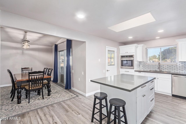 kitchen featuring light wood-style flooring, a sink, appliances with stainless steel finishes, dark countertops, and tasteful backsplash