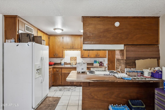 kitchen featuring brown cabinetry, light countertops, a textured ceiling, white fridge with ice dispenser, and light tile patterned flooring