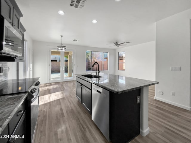 kitchen featuring pendant lighting, an island with sink, sink, appliances with stainless steel finishes, and dark hardwood / wood-style floors