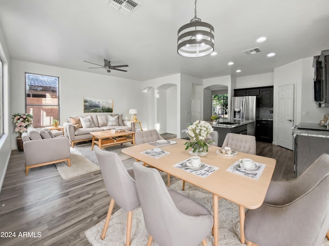 dining area with sink, ceiling fan with notable chandelier, and dark wood-type flooring