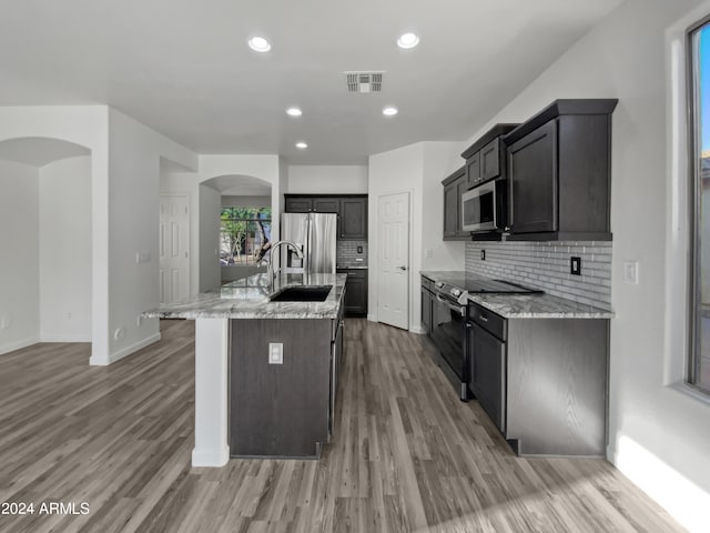 kitchen featuring light stone counters, a center island with sink, stainless steel appliances, and light wood-type flooring