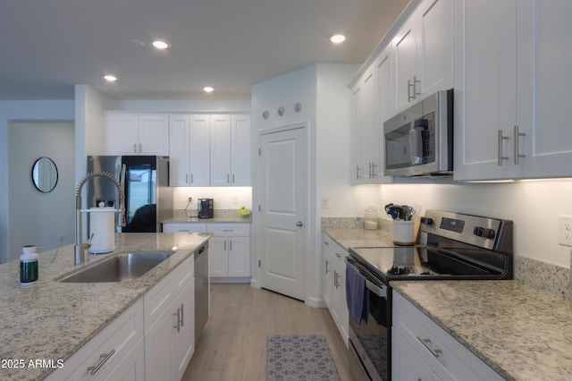 kitchen with sink, white cabinetry, stainless steel appliances, light hardwood / wood-style floors, and light stone countertops