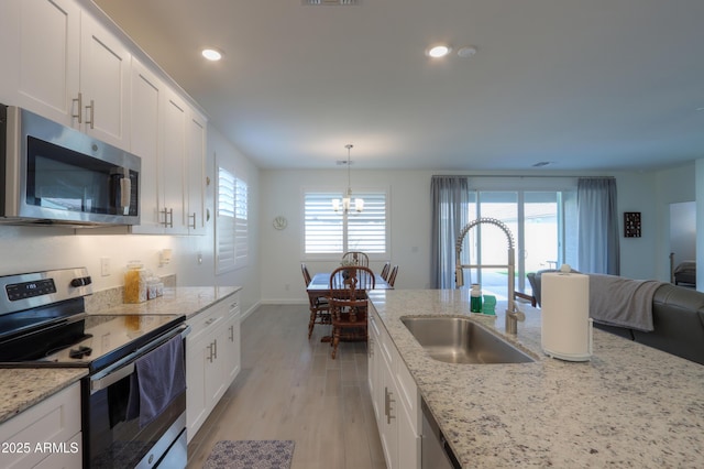 kitchen featuring stainless steel appliances, decorative light fixtures, sink, and white cabinets