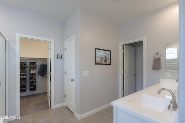 bathroom with double vanity, a spacious closet, baseboards, and a sink