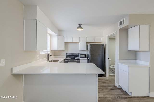 kitchen featuring sink, white cabinetry, kitchen peninsula, wood-type flooring, and black appliances